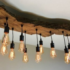 Uma lumin&aacute;ria de teto r&uacute;stica feita de uma grande placa de madeira natural com nove l&acirc;mpadas Edison expostas penduradas em fios pretos, criando uma atmosfera aconchegante e vintage.
