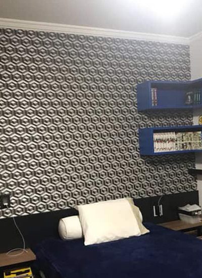 Um quarto moderno com um impressionante papel de parede 3D com padrões hexagonais em preto e branco, uma cama azul adornada com um travesseiro e almofada brancos e elegantes prateleiras azuis montadas na parede exibindo livros e decoração.