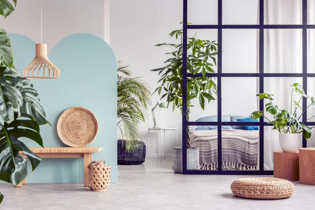 Foto de um quarto com decoração boho chic. No quarto tem uma cama, peças em palha e plantas.