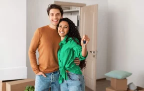 Imagem de um casal feliz mostrando a chave de um apartamento no dia da mudança para ilustrar matéria sobre comprar ou alugar
