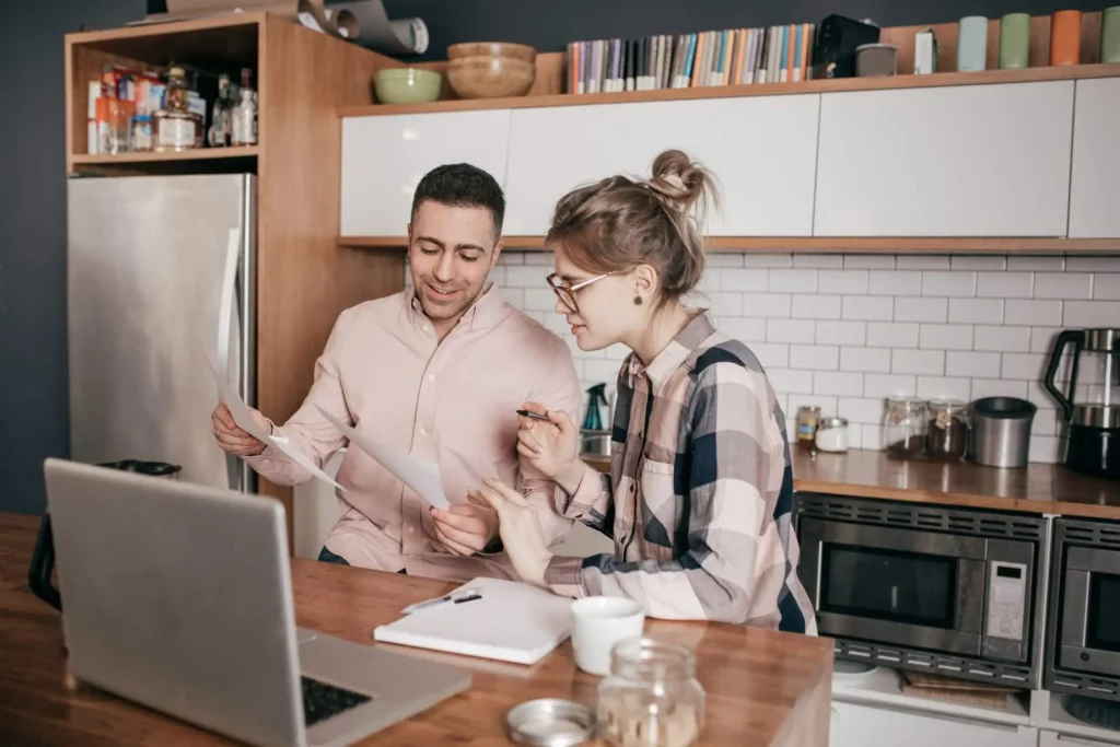 Imagem de um casal em casa analisando papéis e informações em um notebook para ilustrar matéria sobre comprar ou alugar imóvel