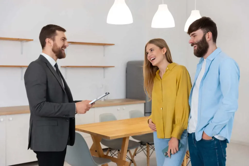 Imagem de um homem de terno segurando uma prancheta sorrindo e conversando com um casal alegre em um escritório moderno e bem iluminado, para ilustrar matéria sobre imobiliária digital.