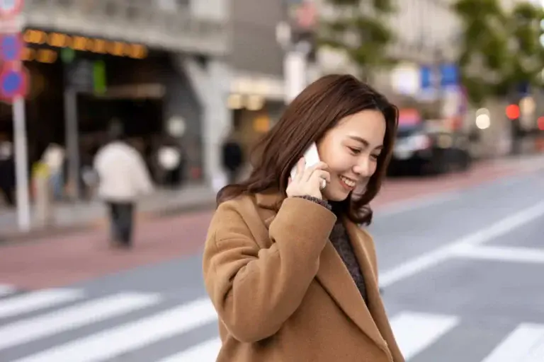 Imagem de uma mulher com roupa de frio atravessando a faixa de pedestre de uma cidade com o celular no ouvido durante uma ligação