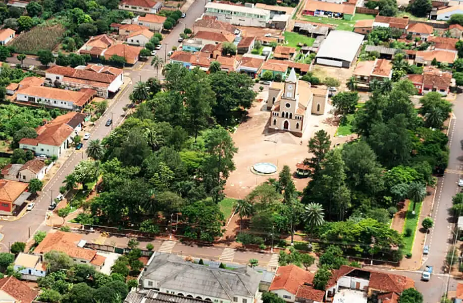 Imagem da vista aérea da praça da cidade de Gavião Peixoto, em São paulo, com uma igreja central, fonte e árvores, cercada por casas de telhado vermelho