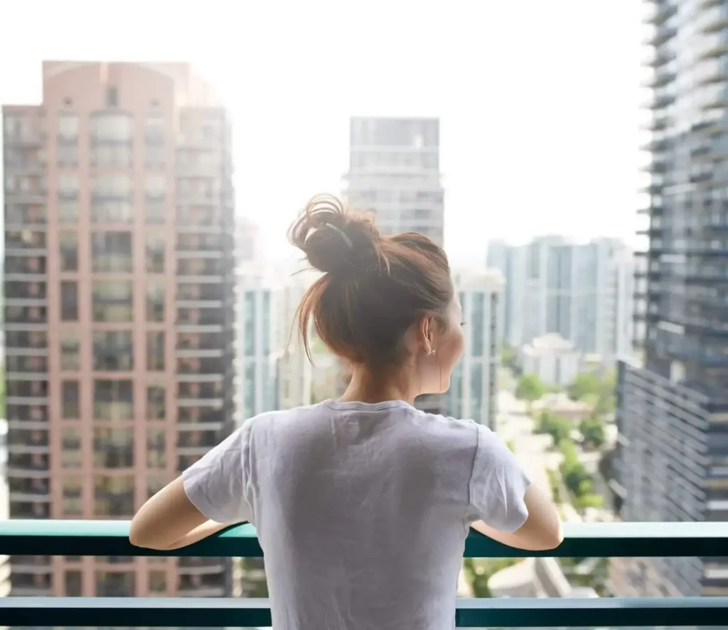 Imagem de uma mulher na varanda de um apartamento observando a vista de prédios a frente para ilustrar matéria sobre o melhor lugar para morar em SP
