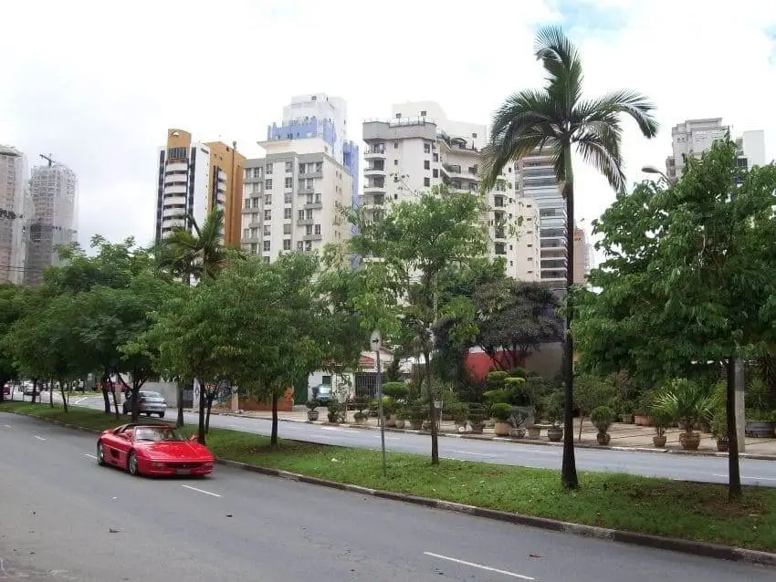 Imagem da vista do bairro Vila Nova Conceição mostra a avenida com um carro passando, vegetação e prédios ao fundo para ilustrar matéria sobre os melhores bairros de SP