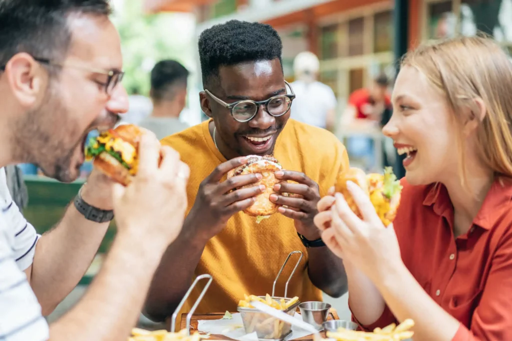 Imagem de três amigos sentados ao redor de uma mesa comendo hambúrgueres