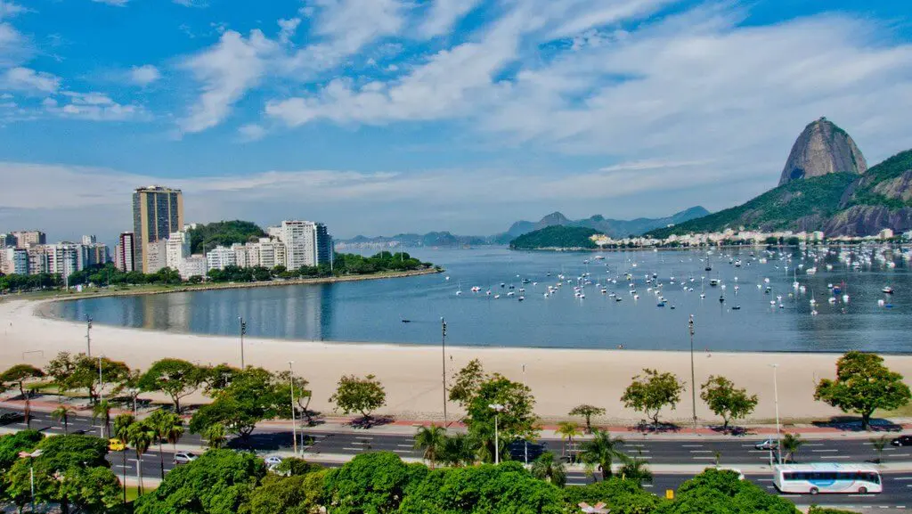 Imagem da vista aérea da Praia de Botafogo mostra mar, faixa de areia, vegetação e prédios ao redor para ilustrar matéria sobre onde morar no RJ