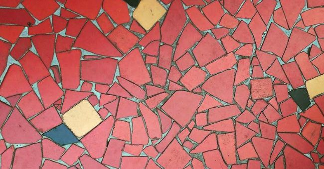 Um padrão de mosaico de azulejos vermelhos de formato irregular, com alguns detalhes em amarelo e preto espalhados pela argamassa cinza, evoca o charme aconchegante de uma Casa de vó.