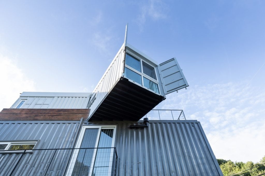 Uma casa moderna feita de contêineres empilhados, com um contêiner superior projetando-se e suas portas abertas, em contraste com um céu azul — um exemplo das Casas dos sonhos de Porto Alegre.