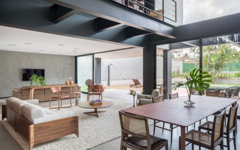 Sala de estar e jantar moderna e aberta, com janelas amplas, móveis neutros, plantas de interior, um tapete e vista para o pátio e a piscina — perfeita para quem busca Casas dos sonhos de Brasília. A luz natural realça a decoração elegante e contemporânea.