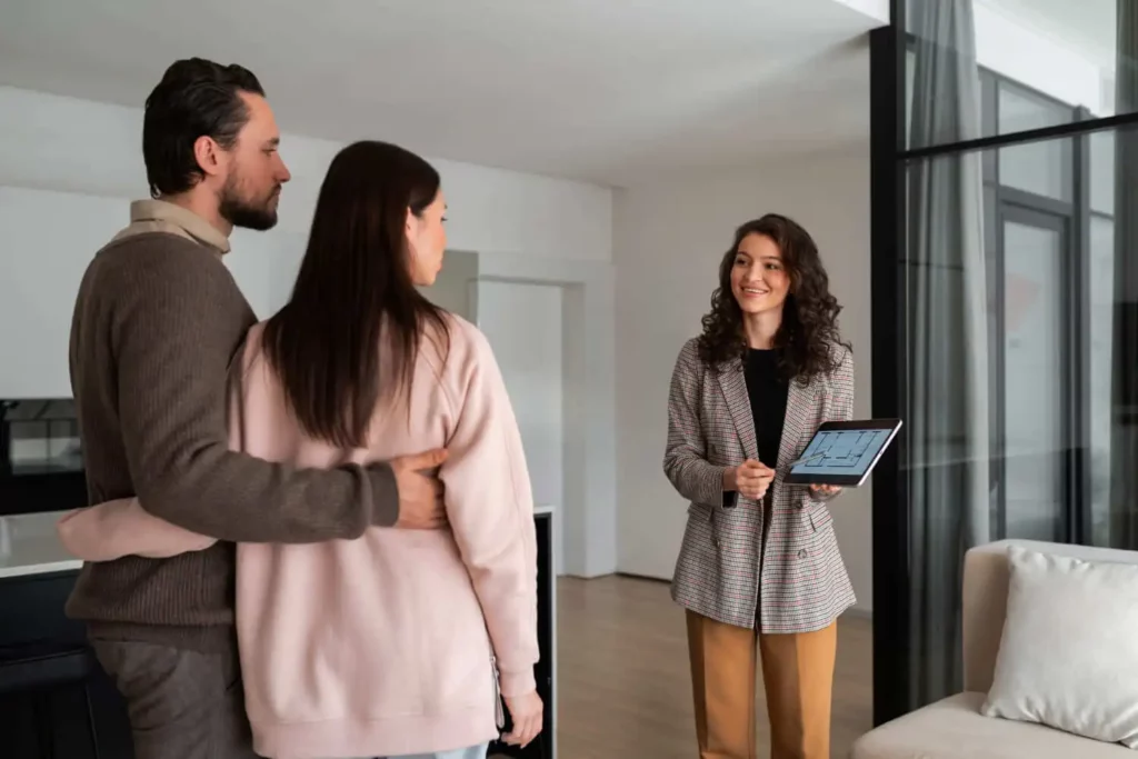 Imagem de uma agente imobiliária segurando um tablet enquanto mostra um apartamento para um casal para ilustrar matéria sobre o que precisa para comprar um apartamento