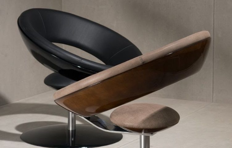 Uma cadeira moderna e circular com assento de couro preto, estrutura externa curva marrom e almofada redonda marrom fica sobre uma base de pedestal prateada — um exemplo icônico de móveis modernistas em uma sala minimalista com piso de cerâmica de cor clara.