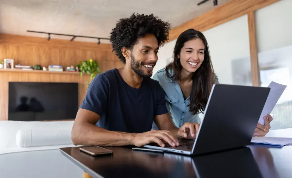 Imagem de um casal formado por um homem e uma mulher mexendo em um notebook em casa para ilustrar matéria sobre quanto custa o seguro fiança