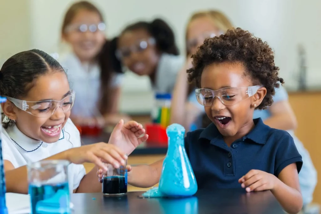 Imagem de duas crianças fazendo um experimento de química em uma sala de aula