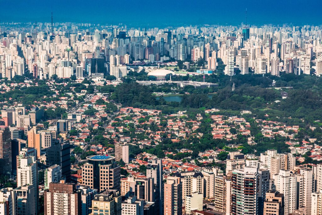 Imagem da vista aérea de Moema, em São Paulo, mostra um denso aglomerado de edifícios altos, casas residenciais e um grande parque verde com árvores e um lago no centro.