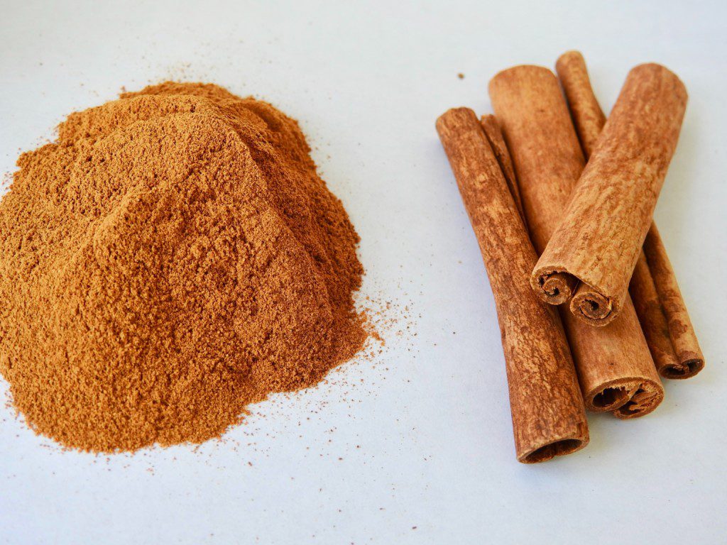 A foto contém no canto esquerdo um pouco de canela em pó e no canto direto, canela em pau