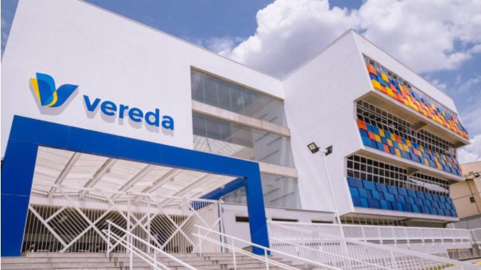 Um prédio branco moderno com "vereda" e um logotipo colorido em azul e amarelo na fachada, exibindo grandes janelas, escadas e painéis multicoloridos. O céu está parcialmente nublado — um destaque entre as escolas em Santo André.