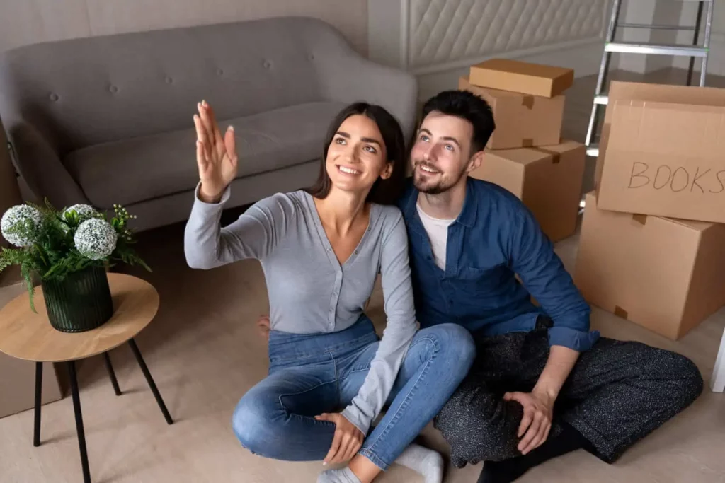Imagem de um homem e uma mulher sentados na sala de um imóvel ao lado de um sofá, uma mesinha de centro e caixas de papelão para ilustrar matéria sobre o que é caução no contrato de aluguel