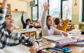 Imagem de crianças sentadas nas carteiras de uma sala de aula com mãos levantadas para tirar dúvida para ilustrar matéria sobre escolas em Osasco