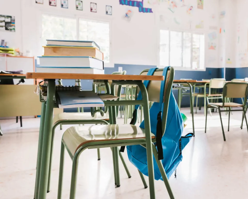Imagem de uma mesa escolar cheia de livros e uma cadeira com uma mochila pendurada para ilustrar matéria sobre as escolas estaduais em Osasco