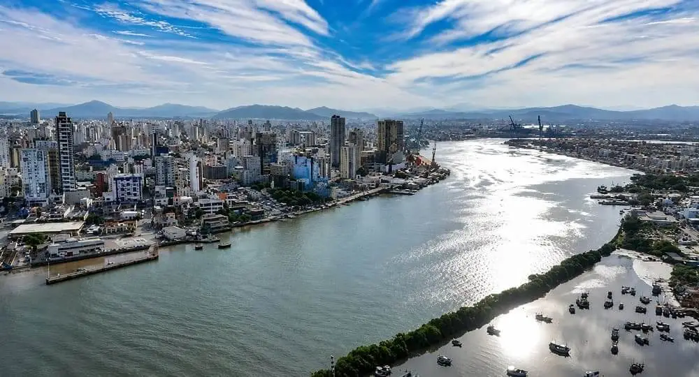 Imagem da vista aérea do Porto de Itajaí, em Santa Catarina, mostra canal aquaviário e prédios ao fundo