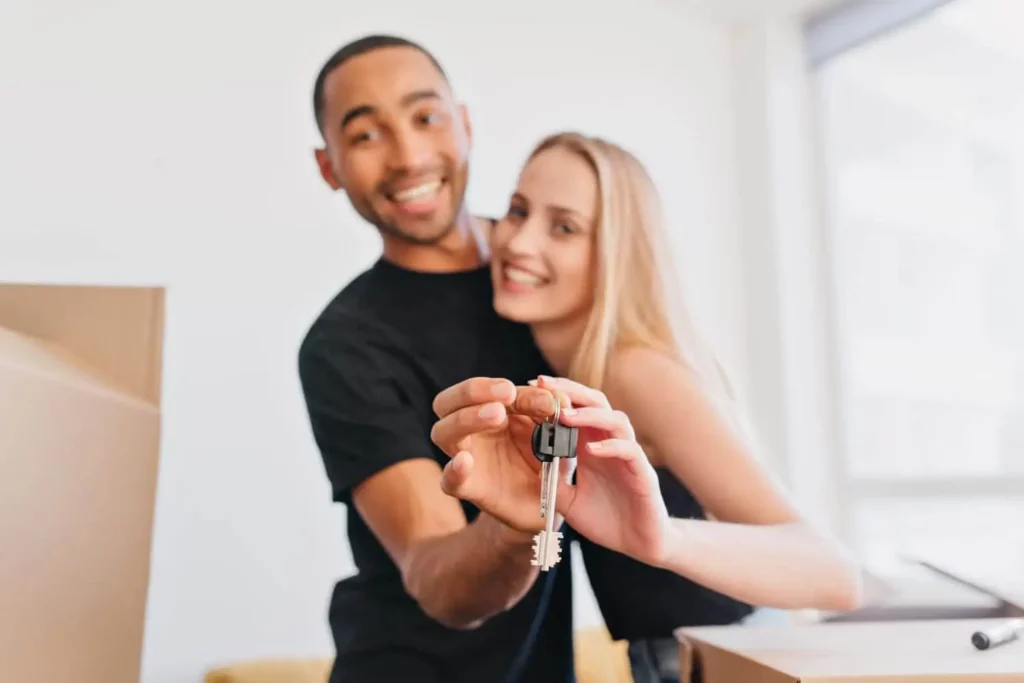 Imagem de um homem e uma mulher abraçados dentro de uma casa enquanto seguram a chave do imóvel para ilustrar matéria que responde a pergunta: caução no aluguel é obrigatória?