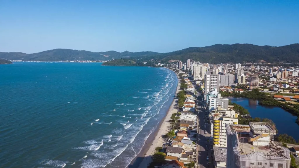 Imagem do litoral de Porto Belo, em Santa Catarina, mostra mar, faixa de areia e prédios para ilustra matéria sobre onde viver em Santa Catarina