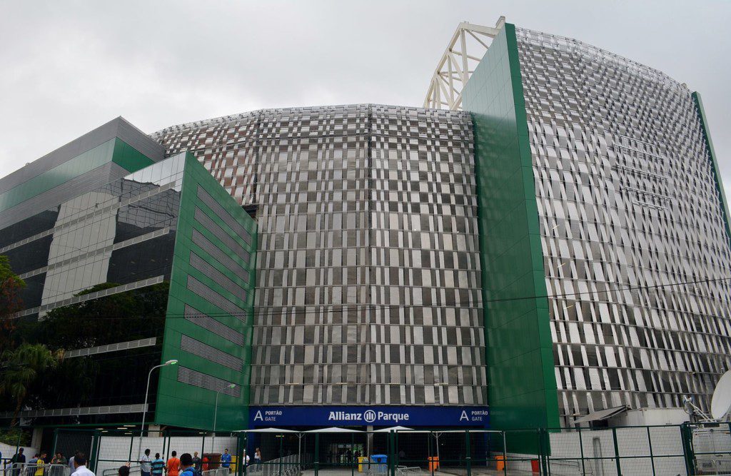 Um grande estádio moderno com painéis externos verdes e prateados e uma placa com os dizeres “Allianz Parque” acima da entrada, localizado perto da estação de metrô Barra Funda, com pessoas reunidas do lado de fora do portão principal em um dia nublado.