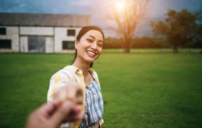 Imagem de uma mulher sorridente em um gramado verde, segurando a mão de alguém e olhando para a câmera, para ilustrar matéria sobre o que é CIB.