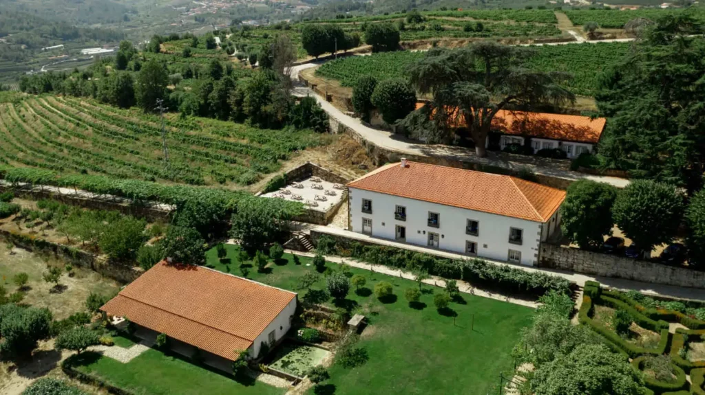 Imagem da vista aérea de uma propriedade rural com edifícios brancos e telhados vermelhos cercados por jardins verdejantes, vinhedos e estradas sinuosas em uma paisagem rural montanhosa, para ilustrar matéria sobre o que é o documento NIRF