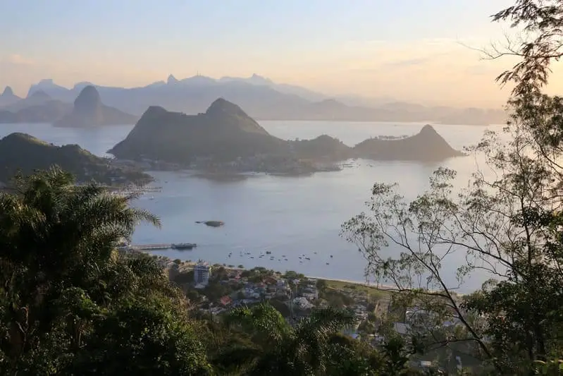 Imagem costeira de Niterói mostra um mar com águas calmas, ilhas, montanhas distantes e céu com cores pastéis suaves