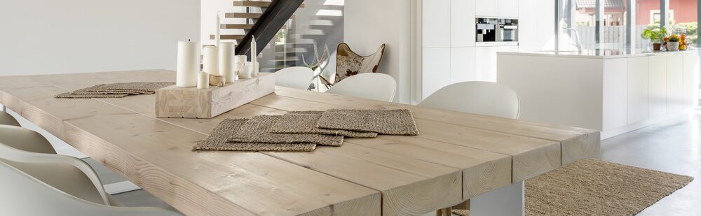 Foto que ilustra matéria sobre decoração de mesa mostra uma mesa de madeira com seis lugares, com destaque para um jogo de velas como centro de mesa.