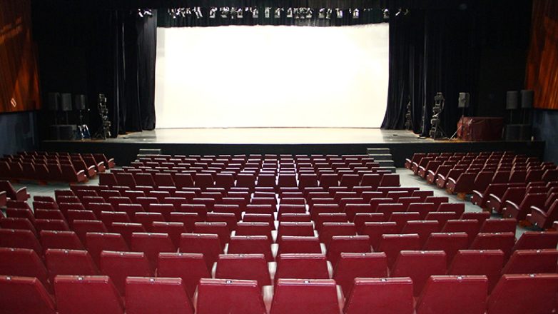 Fileiras de assentos vermelhos vazios de teatro dão para um amplo palco com fundo branco e cortinas pretas em um auditório espaçoso, um local convidativo para eventos e apresentações culturais — perfeito para quem busca O que fazer em São José dos Campos.