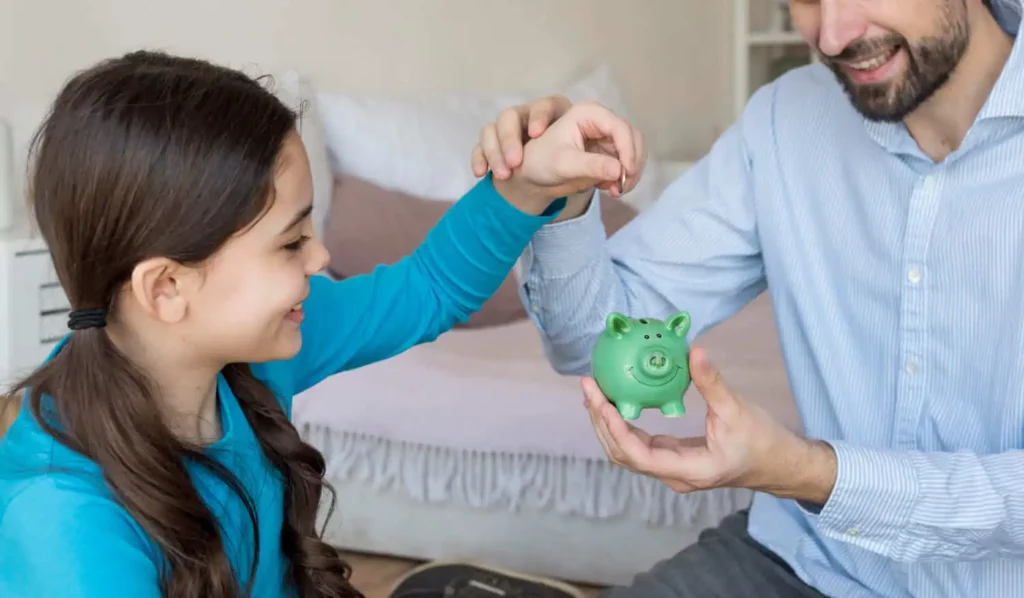 Imagem de uma criança colocando uma moeda em porquinho que o pai está segurando para ilustrar matéria sobre como financiar um imóvel sem entrada