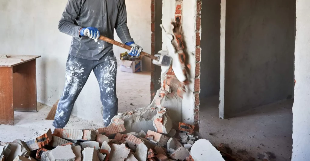 Imagem de um mestre de obras quebrando as paredes de um imóvel para ilustrar matéria sobre quanto custa uma reforma de apartamento