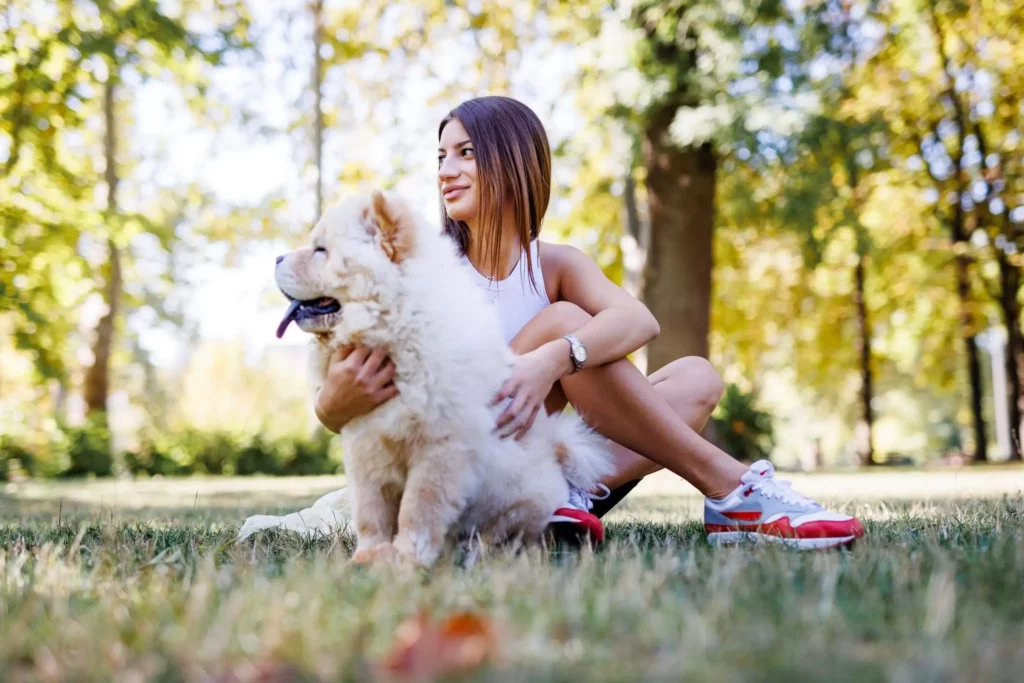 Imagem de uma mulher sentada no gramado com um cachorro branco para ilustrar matéria sobre os melhores parques de Goiânia
