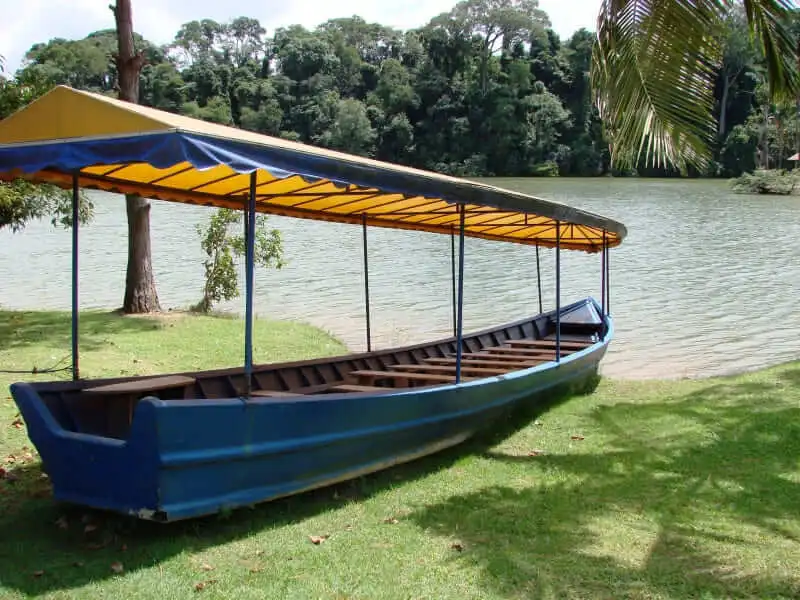 Imagem de um barco azul com uma cobertura amarela eem um terreno gramado à beira de um lago da Represa João Gasparini, cercado por árvores, para ilustrar matéria sobre o que fazer em Vinhedo com crianças