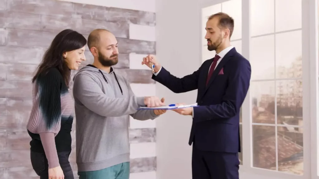 Imagem de um homem de terno entregando as chaves da casa e uma prancheta a um casal sorridente para ilustrar matéria que explica se registro e escritura são a mesma coisa.