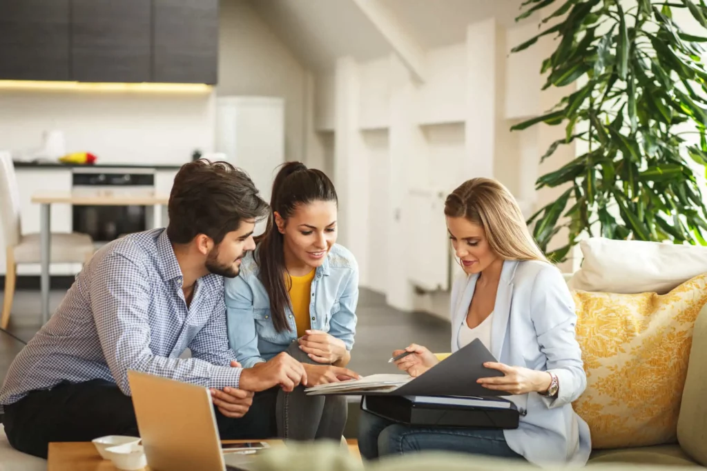 Imagem de um casal formado por um homem e uma mulher conversando com uma agente imobiliária para ilustrar matéria sobre como funciona o repasse de financiamento