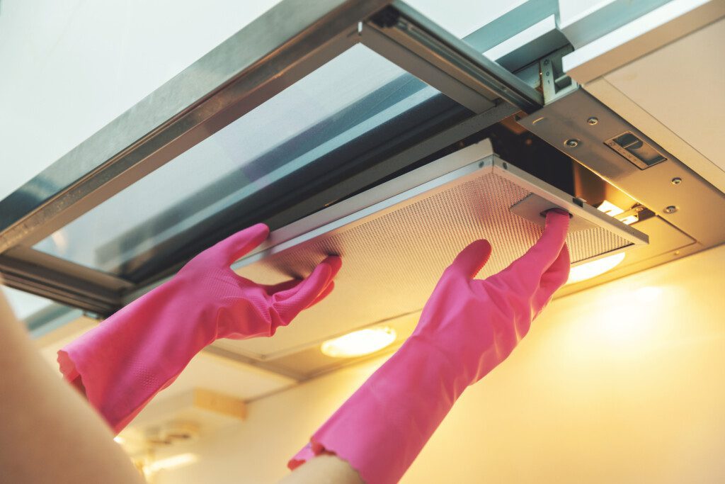 Imagem de duas mãos vestidas com luvas descartáveis de limpeza pressionando um botão de uma coifa de inox