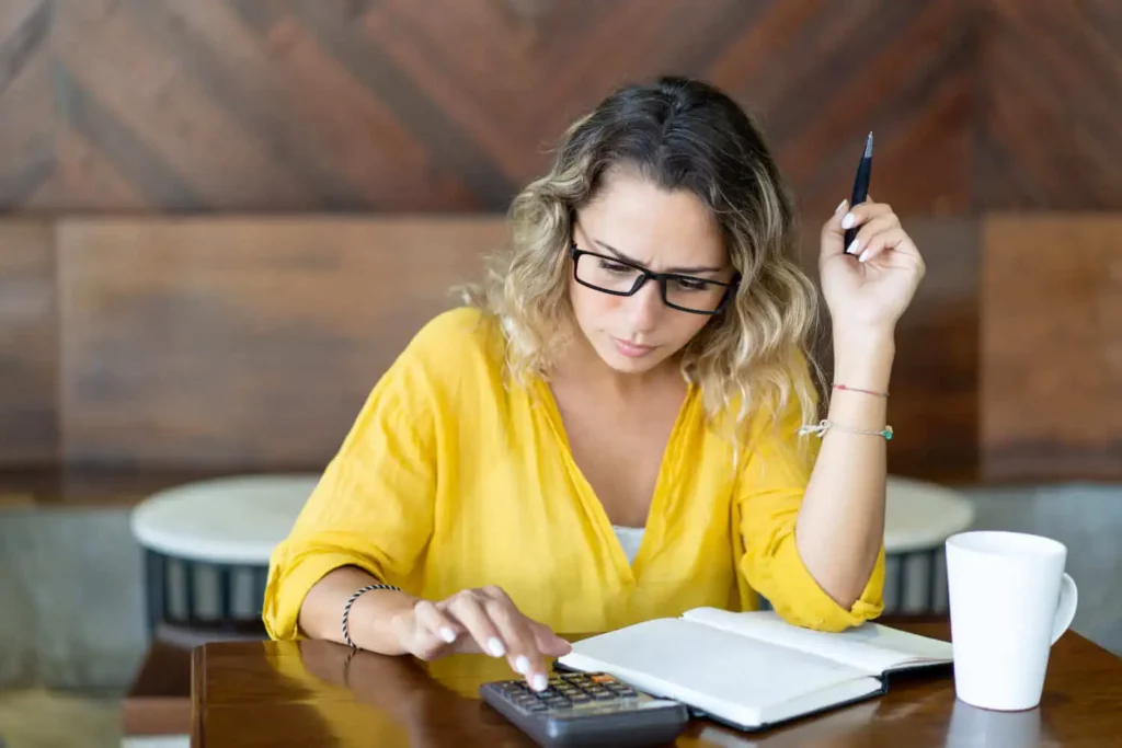 Imagem de uma mulher com cara de séria fazendo cálculos em uma calculadora sobre uma mesa para ilustrar matéria sobre o que é ação de consignação em pagamento