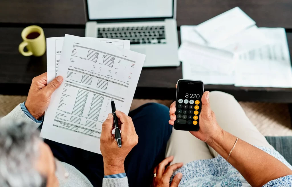 Imagem de duas pessoas fazendo contas com base nas informações de um papel e nos cálculos da calculadora de um celular para ilustrar matéria sobre o que é saldo devedor