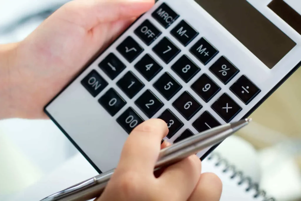 Imagem de uma mão digitando em uma calculadora enquanto segura uma caneta para ilustrar matéria sobre como o saldo devedor é calculado?