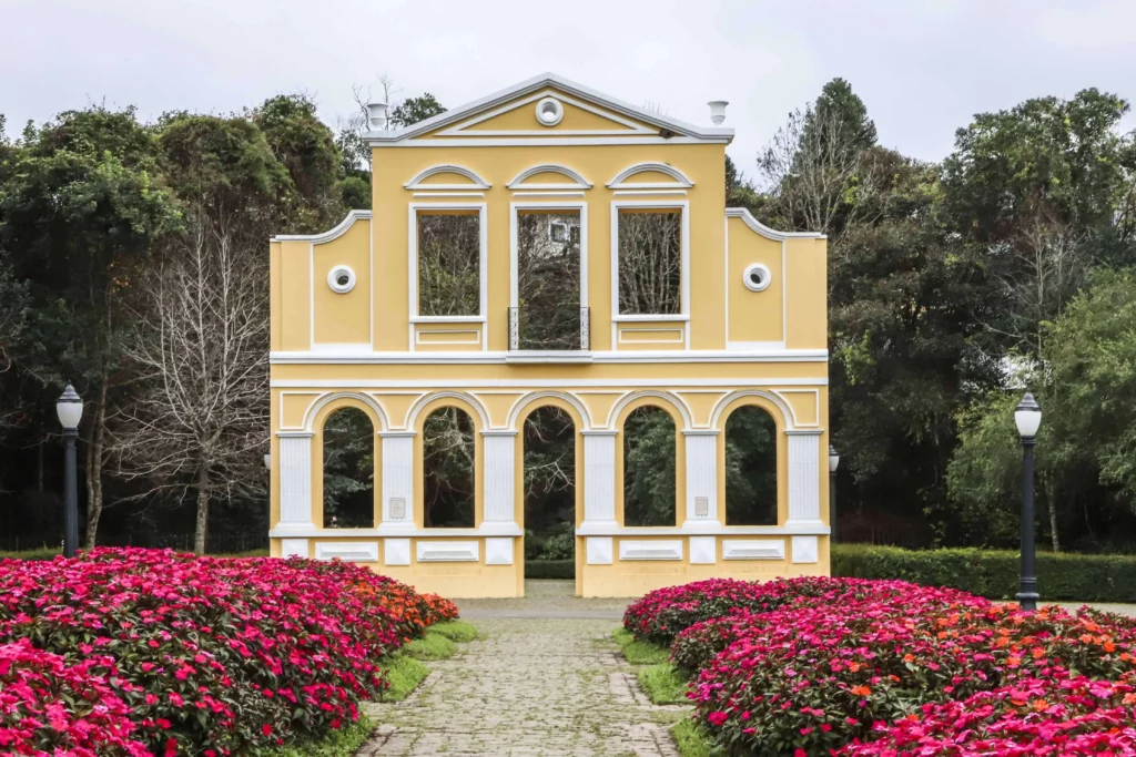 Imagem do Bosque Alemão mostra canteiro com flores e uma construção que remete à arquitetura alemã para ilustrar matéria sobre parque em Curitiba