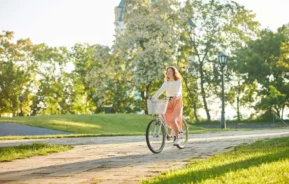 Imagem de mulher jovem andando de bicicleta em um parque no fim da tarde para ilustrar matéria sobre os parques em Curitiba