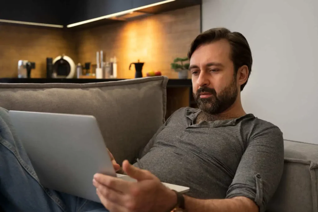 Imagem de um homem sentado no sofá da sala de casa com um notebook no colo para ilustrar matéria sobre o valor do m² em São Paulo