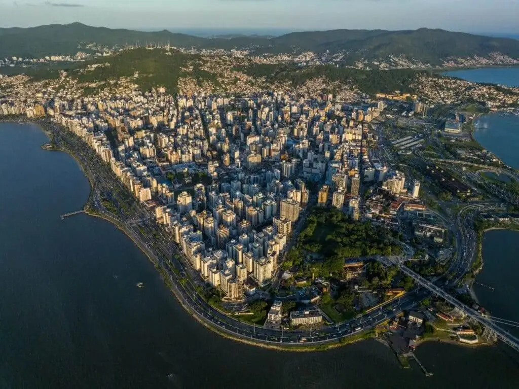 Imagem da vista aérea de Florianópolis mostra a cidade com prédios altos cercada por água para ilustrar matéria sobre as cidades com menor custo de vida em Santa Catarina