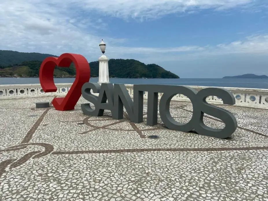 Imagem de um letreiro com a palavra “Santos” em frente ao mar para ilustrar matéria sobre o custo médio de vida em Santos