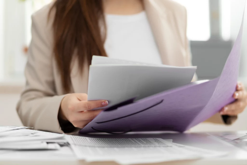 Imagem de uma mulher segurando documentos sentada à mesa para ilustrar matéria sobre os documentos necessários para comprovar renda no consórcio